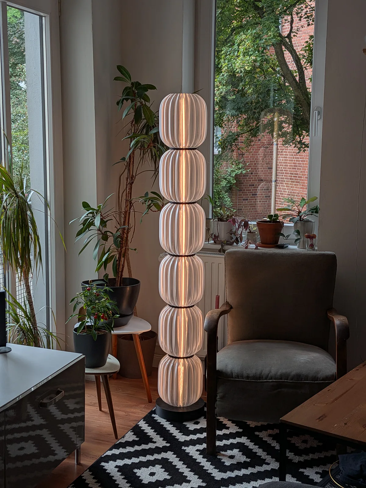 Dieselbe Stehlampe aus etwas größerer Entfernung, zwischen Zimmerpflanzen und einem Sessel.
